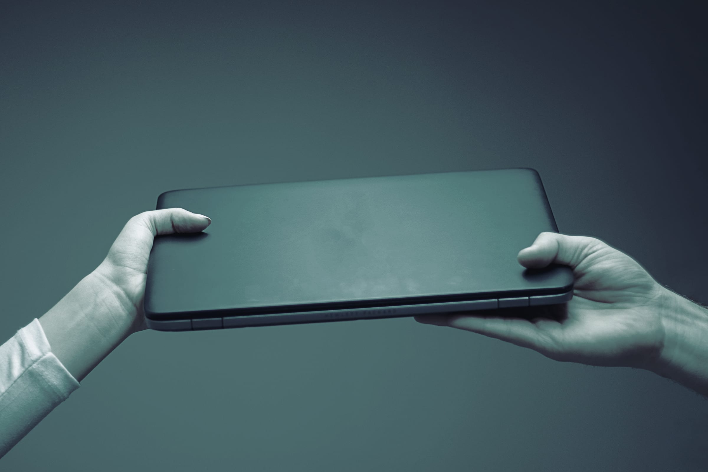 Two hands passing a closed laptop.