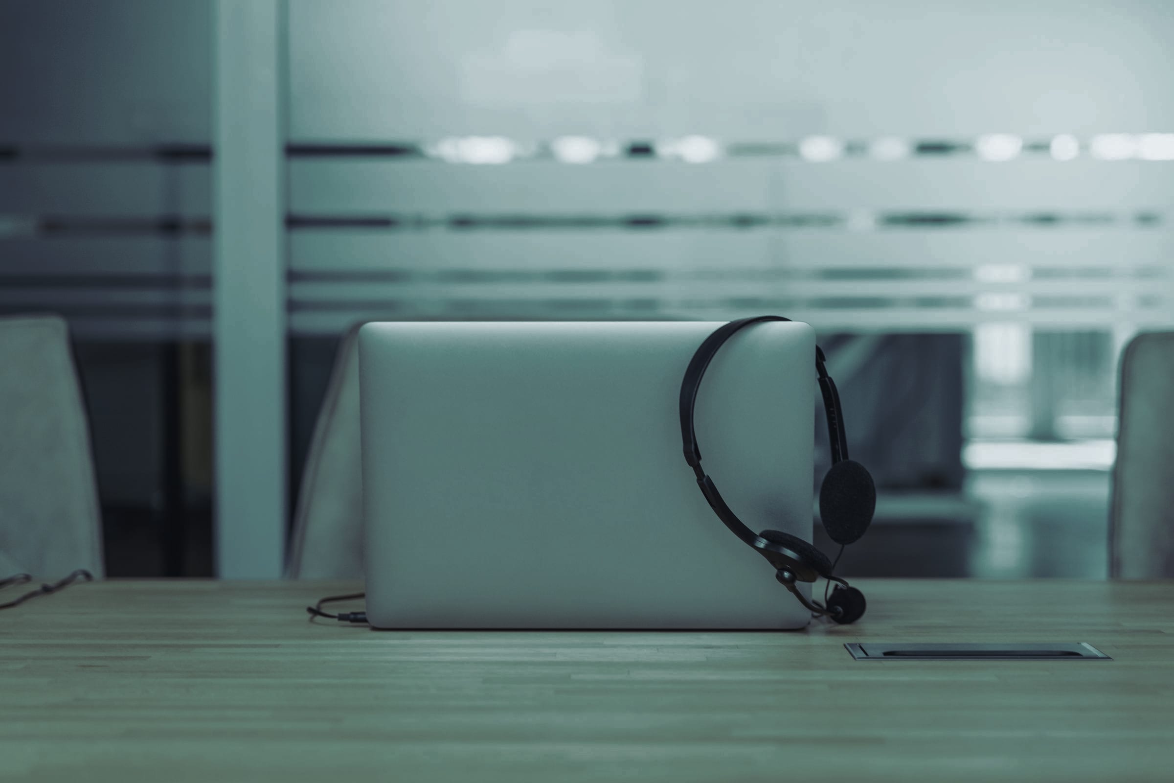 A closed laptop with a headset on an empty desk.